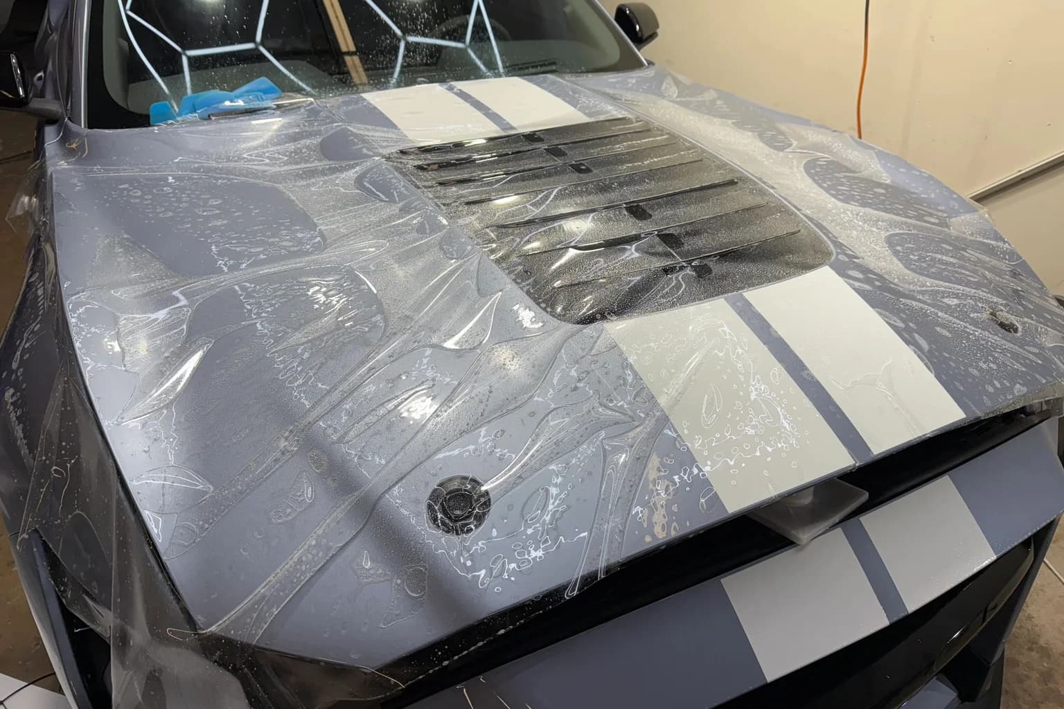 Clear paint protection film being wet-installed across a striped vehicle hood at AutoWorks